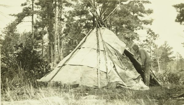 Carl standing and looking through the entrance of a tipi (teepee) near Rainy Lake.