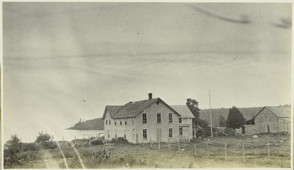 View across field towards the Chicago Bay Boarding House. The lake is in the background on the left. Chicago Bay, Minnesota, is now called Hovland.