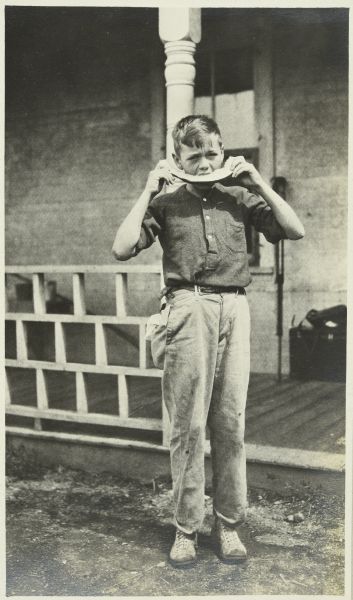 John "Jack" Greene standing in front of a porch eating a slice of watermelon.