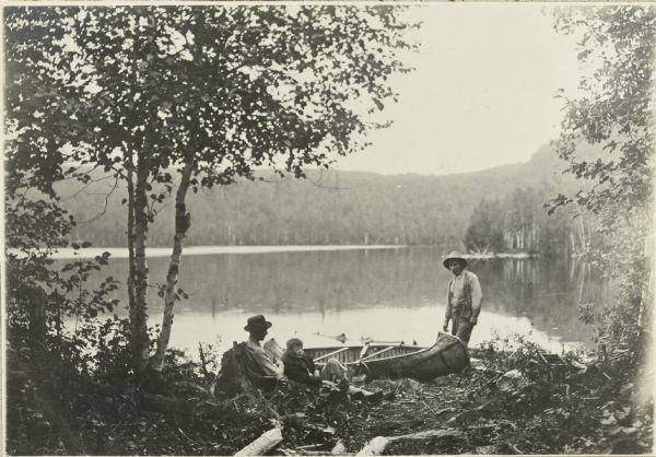 From left to right: Clay, Jack, and Edwin Kugler are next to a canoe on the shore of Pine Lake.
