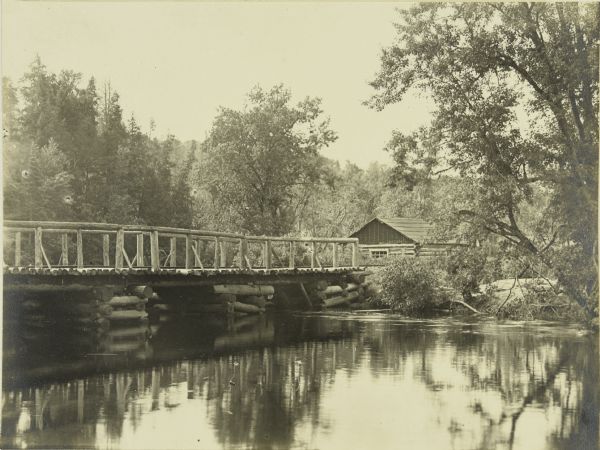 View across water from shoreline towards a railroad bridge at a camp near Marenisco, Michigan. There is a log building on the opposite shoreline.