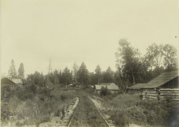 A view down a rustic road of "Mail Camp 8" near Marenisco, Michigan, including a number of log cabins.