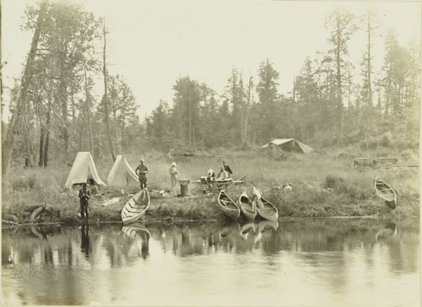 A view across water towards Camp 2, showing tents, canoes, and The Gang.
