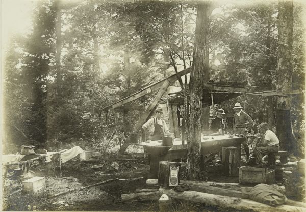 The men are gathered around the mining camp table at their camp on Presque Isle River.