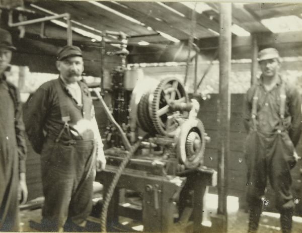 Several men standing next to gears and machinery inside a diamond drill outfit.