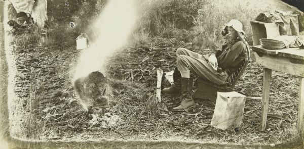 Charles is sitting near the table at the fourth camp of the trip. In from of him is either a blazing campfire or photographic light fog on the negative of this image. In the journal, this image is captioned, "Home and Mother."