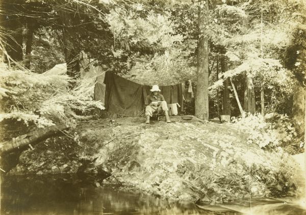 The fifth camp of The Gang's trip on the bank of the Presque Isle River. One of The Gang (probably Howard T.) is reading a book.