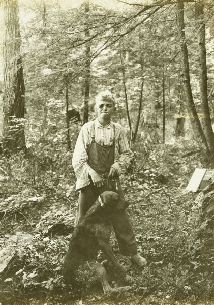 Carl posing as a "Havud Boy" (Harvard), with his dog Nimrod in the woods. Carl is wearing an eye patch and has what appears to be a cigarette in his mouth.