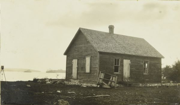 A small house near a lake in Winton. There appears to be a large format camera set up to the left of the house.