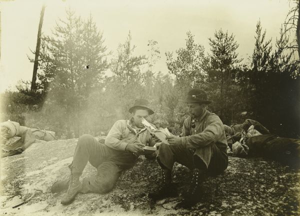 Fred Carr and Bill Marr reading a map together while sitting on the ground.