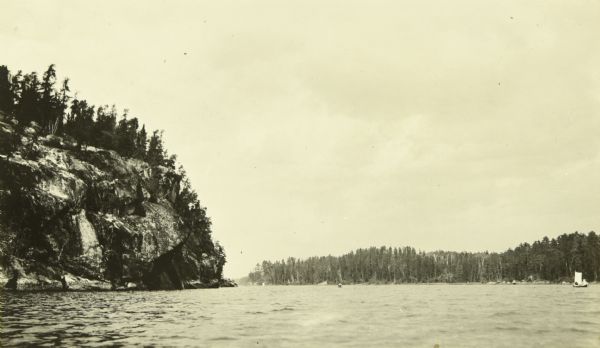 A view across either Basswood Lake or Crooked Lake with a large rock formation on the left and trees on the opposite shore. 