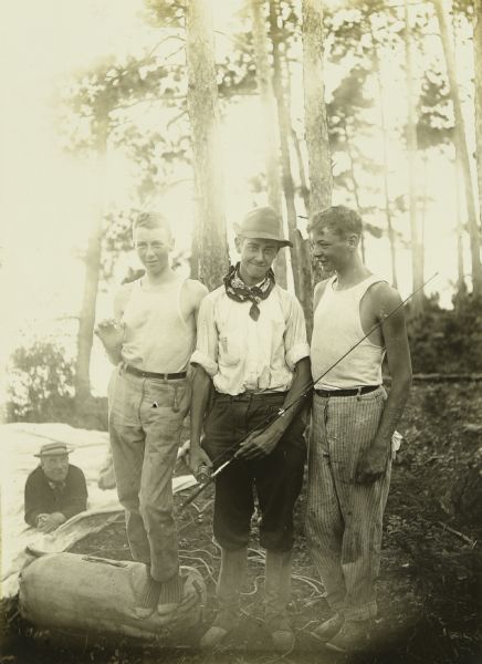 The three youngest travelers of The Gang posing together. From left to right are: Charles Isley, Fred Hanson, who is holding a fishing pole, and Howard T. Greene. Billy Mac is relaxing on a tarp behind the boys.