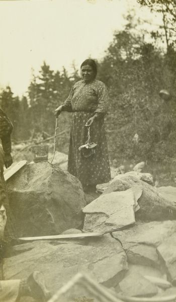 An Indian woman standing on rocks holding two containers of blueberries.