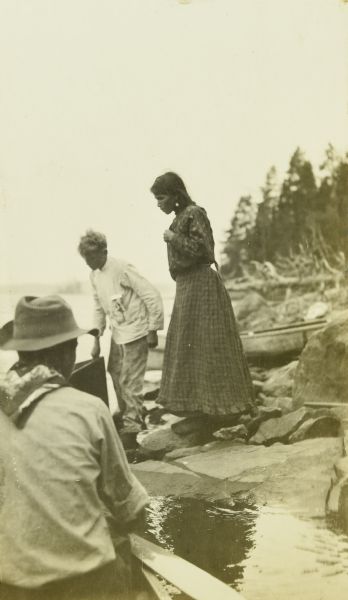 Carl standing next to an Indian woman who is selling blueberries to The Gang. One of the men is in the foreground. Lac La Croix is in the background.