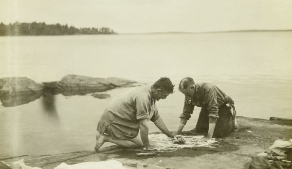 Bill Marr, on the left, and Howard "Dad" Greene washing their clothes with soap on a rock by the lake.