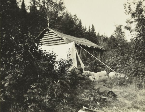 The Gang's tent and camp is set up next to an abandoned shack. Their bed rolls are on the ground near the tent.