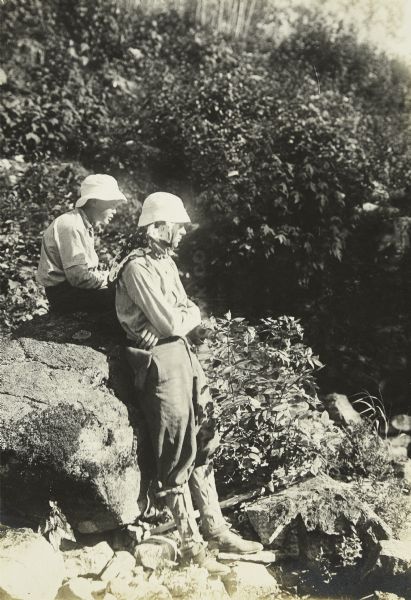 Jack and William Norris resting during a portage. Jack is sitting on a large rock and William is leaning against it.
