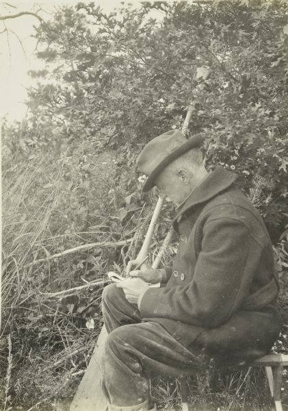 Howard Greene ("Dad") sitting on a stool outdoors writing in a notebook.