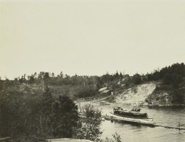An elevated view of a steamboat on Rainy Lake near Kettle Falls. In the background is borrow pit for construction of Kettle Falls Dam.