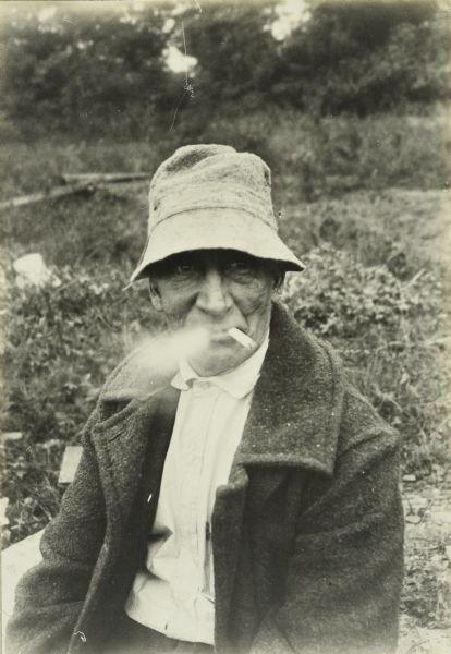 A candid portrait of Doc Copeland sitting outdoors. He is wearing a wool coat and is smoking a cigarette.
