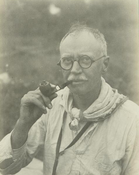 A candid portrait (possibly a self-portrait) of Howard Greene, who is known to The Gang as Dad. He is wearing eyeglasses and is smoking a pipe.