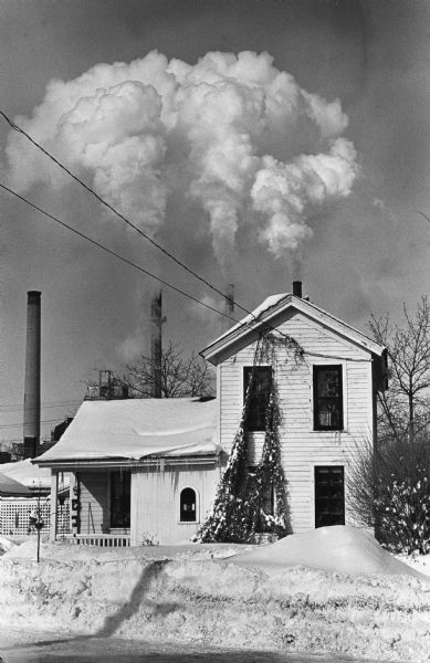 High humidity and low temperatures cause massive steam clouds to billow from the stacks of Wisconsin Power and Light Company behind a house on Jenifer Street.