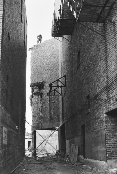 View down the alley at the back of the Capitol Theatre on State Street towards a construction worker standing on the roof while working on renovations.