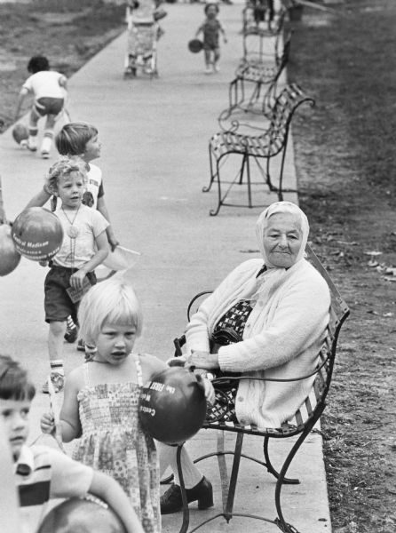 An elderly woman sitting on a park bench is watching the children's parade as part of the Week of the Young Child celebration. The Week of the Young Child is an annual event celebrated nationally to bring attention to the needs of young children and to introduce parents to early childhood programs that serve those needs.