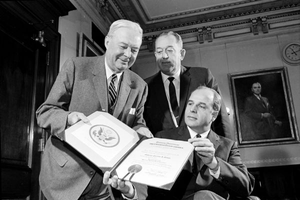 Governor Gaylord Nelson (right) receives his commission as honorary state chairman of the 1961 Savings Bond Drive from Harold F. Dickens, Milwaukee, who is the director of the United States Treasury's Savings Bond division. Looking on (center) is I. W. Lackore, executive director of the Madison Chamber of Commerce and named Dane County volunteer chairman.