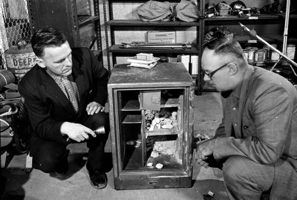 Safe robbers escaped with $1,000 in cash, $2,000 in checks, and several wrist watches when they stole a large safe from the Holmes Tire and Supply Company on Syene Road. Captain Earl Sorenson, left, and Undersheriff Jack Leslie are searching for fingerprints and tool marks on the stolen safe which was found empty later in the day.