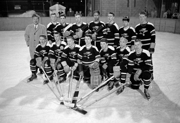 Group portrait of the 14 players for the Madison Hawks boys hockey team, who were the undefeated champions of the Southern division in the State League. Their coach, shown left, is John Riley.