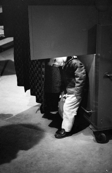 "We Saw You Performing Civic Duty." A child is peering out from beneath the curtain of a voting booth as his parent votes.