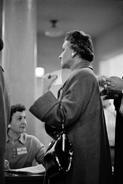 "We Saw You Performing Your Civic Duty" in the spring 1961 elections. A pensive woman voter, her slip in hand, waits a turn in the booth.