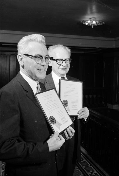 Two men posing holding plaques. The original caption states: "Happy winners, Arthur Behling, Milwaukee, left, and G.D. Simonds, Clintonville, displaying award plaques presented to them at a banquet of the Wisconsin Society of Professional Engineers here (at Hotel Loraine in Madison). Behling was named 'Engineer of the Year.' Simonds received an award for the FWD Corp., Clintonville. Simonds is engineering vice-president of the firm."