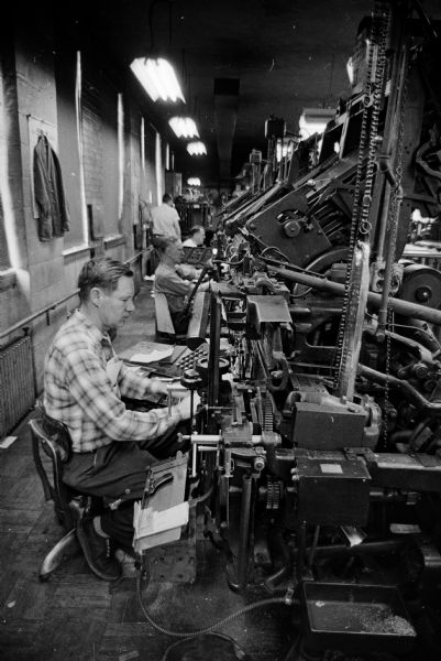 Linotype workers sitting at individual stations in the Wisconsin State Journal building.