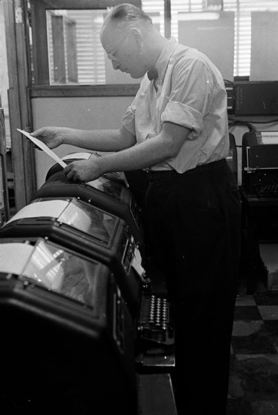 A worker at the Wisconsin State Journal building reading copy from a teletype machine.