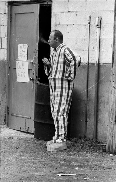 1,500 Cub Scouts, Boy Scouts, Explorer Scouts and their adult volunteers in the Four Lakes Council participated in circus performances at the Dane County Fairgrounds. Here a father in costume is standing at an open doorway and smoking, while waiting for the show to start.