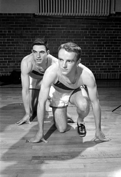 John Huston (left) and Jim Connors, Edgewood high school trackmen, performing stretches. They will compete in the Edgewood Relays in the Camp Randall Memorial building.
