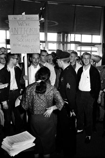 U.W. students protest a rally by the Wisconsin Socialist Club, hosts of an event at the Wisconsin Union theater supporting Fidel Castro and protesting the recent abortive American invasion of Communist Cuba. Here protesting anti-Castro students speak to a Socialist club supporter and a campus policeman at the entrance of the theater.