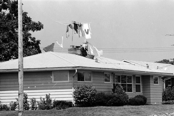 Street view of a ranch-style house with a person on the roof who appears to be hanging laundry on a television aerial.