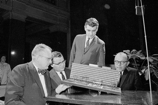 Harold Ames, sitting at center, looking over a model of the State Office building planned for the Hill Farms which was part of the honor awards exhibit of Wisconsin architecture at the State Capitol. Looking on are three Madison winners: Carl Gausewitz (left), Robert Cashin (standing), and Charles Woehrl (right).