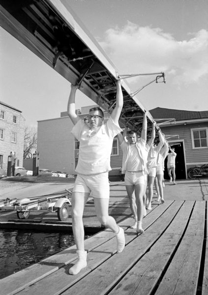 The University of Wisconsin varsity crew preparing to launch its shell on Lake Mendota for a workout. Visible (L-R) are Don Erbach and Phil Monk.