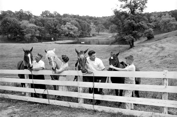 Stanley Herrling (left), his wife, and sons Greg and Mark are each standing next to a horse at a fence bordering the pasture. This is one of a series of photographs of a rural Cross Plains farm which was purchased 6 years ago by Stanley Herrling and returned to family ownership after a period of 40 years. The Herrling family has worked to build a comfortable home and restore the farm's soil, forest, and wildlife.