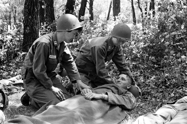 Pfc. Richard Sroda, a public information specialist with the 32nd Division, was the photographer and Sp4 David Gordon, public information specialist for the 44th General Hospital, did the photography and story for this article. Both are Wisconsin State Journal staff members attending summer camp at Camp McCoy. During the mass casualty drill, Capt. Ann Odorico, 122 E. Gilman St. and Capt. Helen Jean MacGregor, 219 Clifford Ct., attend to a patient with a simulated hemorrhage, Sp5 Nathan J. Sherven, Mt. Horeb. Capt. Odorico is a nurse at the Veterans Administration hospital and Capt. MacGregor is on the staff at University Hospitals.