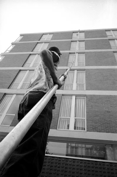 Madison Inn employee Allen Wheeler using a window-washing brush attached to 60-foot long handle with a thin hose which carries soap and water threaded through it to wash the 135 windows in the building at 601 Langdon Street.