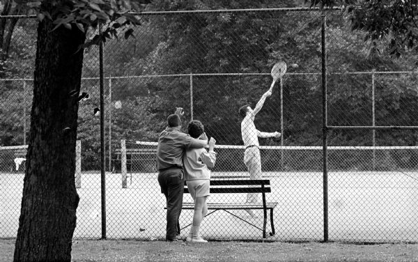 A couple watching a man play tennis at the Tenney Park tennis court.   






