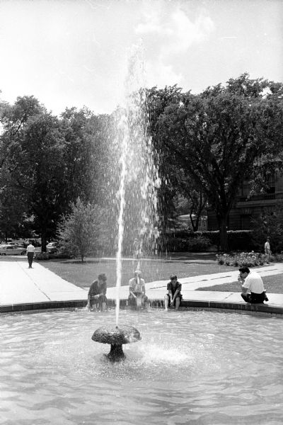 Two University of Wisconsin students cool off in the Library Mall water fountain between the University Library and the State Historical Society building. Shown (L-R) are Ed Sasser, 5521 Dahlen Drive, and Jim Spurley, 147 Craig Avenue. Ed Stein is taking a picture of the boys.