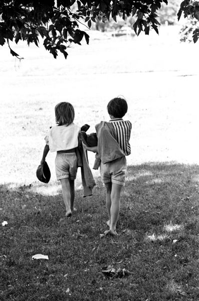Two children walking home carrying their costumes following a Dress Up Day celebration at a city playground.