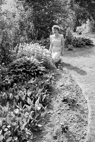 Catherine Barber of the West Side Garden Club, a certified flower show judge, is shown kneeling in the midst of a garden of flowers.