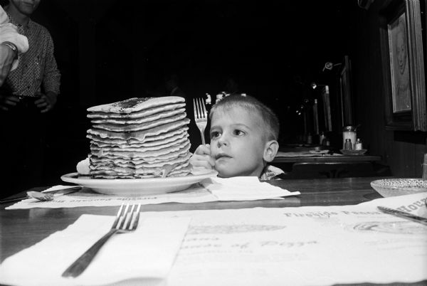 Holding a fork and gazing at a plate piled high with pancakes during an open house and party at the Fireside Pancake House, 625 State Street, is Jeffery Duane, 6. The event is sponsored by the restaurant and United Cerebral Palsy of Dane county for children with cerebral palsy and their parents.